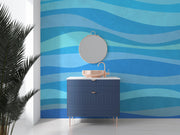 Modern blue wave wall mural with abstract wave patterns in shades of blue, decorating a bathroom with a stylish vanity, round mirror and a potted plant.