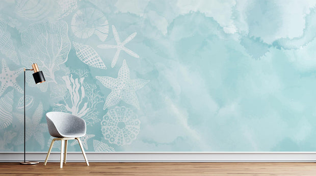 Coastal seashell wall mural and wallpaper with white starfish, coral and seashell illustrations on a soft aqua watercolor background, styled in a modern living room.