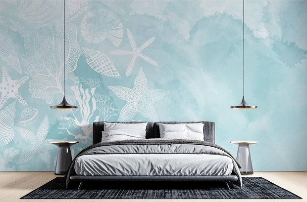 Coastal seashell wall mural and wallpaper with white starfish, coral and seashell illustrations on a soft aqua watercolor background, styled in a modern bedroom.