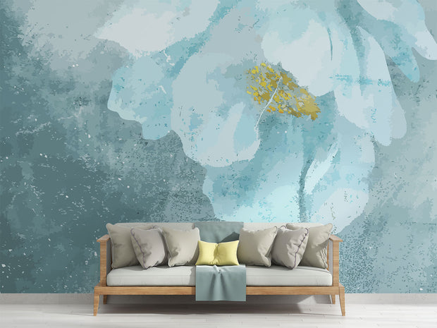 A modern living room with a Blue Floral Watercolor Wall Mural, featuring a delicate oversized flower in teal and gold hues. A wooden sofa with plush neutral and pastel pillows complements the serene aesthetic, creating a cosy and elegant space with a soft, artistic ambience.