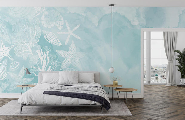 Coastal seashell wall mural and wallpaper with white starfish, coral and seashell illustrations on a soft aqua watercolor background, styled in a modern bedroom.