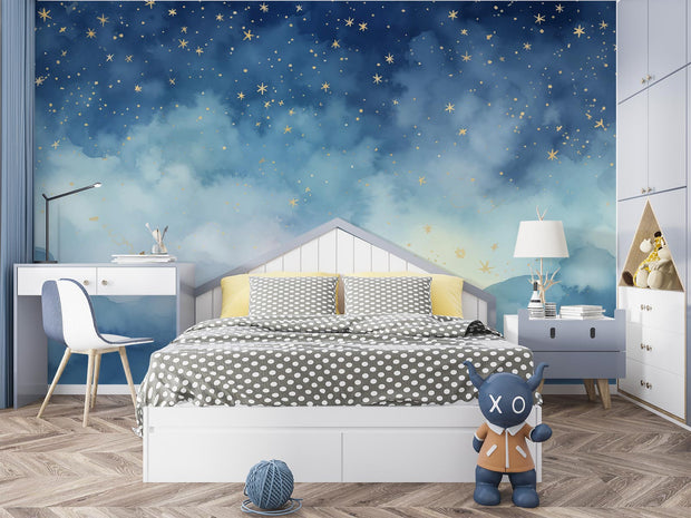 Starry night wall mural featuring a watercolor-style sky in deep blue tones with golden stars, decorating a cozy children’s bedroom with a white bed, desk and playful decor.