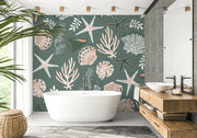 Coastal wall mural featuring starfish, seashells, coral reefs and marine plants in soft pastel tones on a muted green background, decorating a modern bathroom with a freestanding tub.