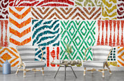 Colorful tribal pattern wall mural with teal, orange, and green geometric designs, styled in living room with two chairs.