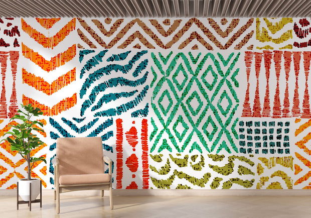 Colorful tribal pattern wall mural with teal, orange, and green geometric designs, styled in living room with a blush chair.