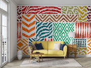 Colorful tribal pattern wall mural with teal, orange, and green geometric designs, styled in living room with a yellow sofa.