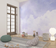 Dreamy cloud-themed wall mural with soft purple hues and fluffy white clouds, decorating a modern children's room with cosy accents, toys and a stylish rug.